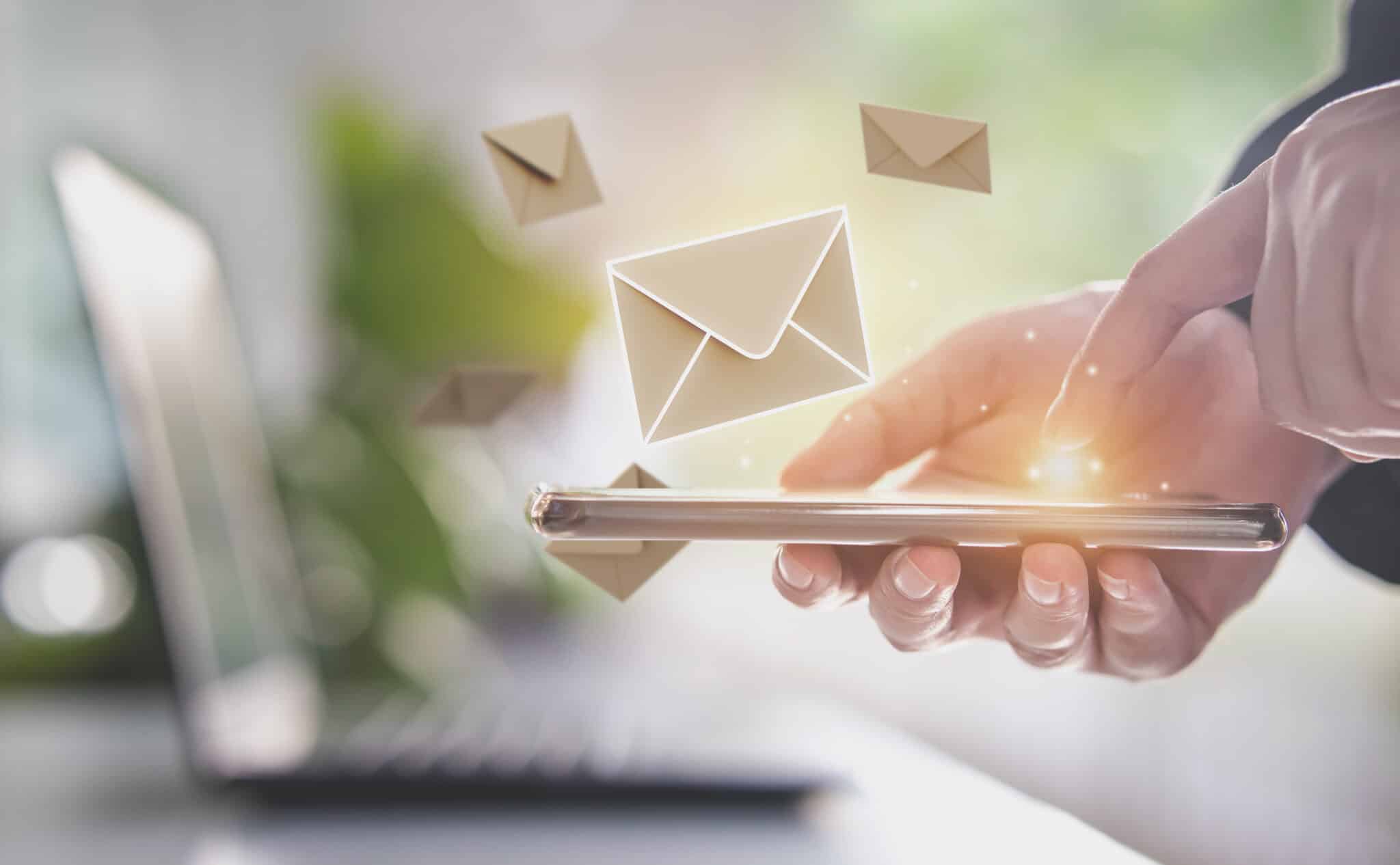 A hand holding a smartphone sending emails